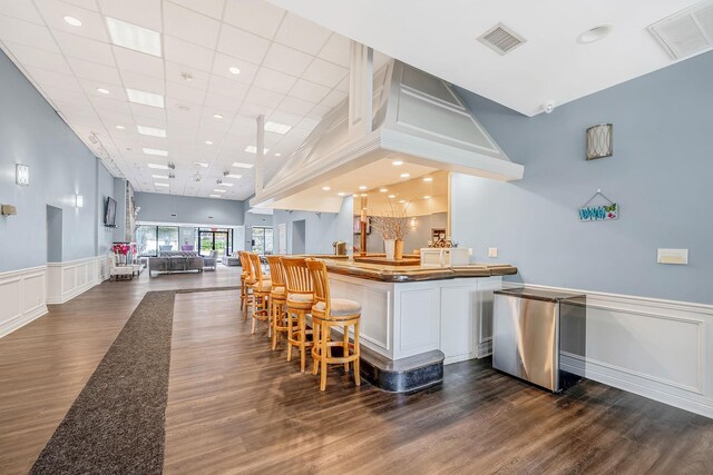 bar with visible vents, refrigerator, dark wood finished floors, and a decorative wall