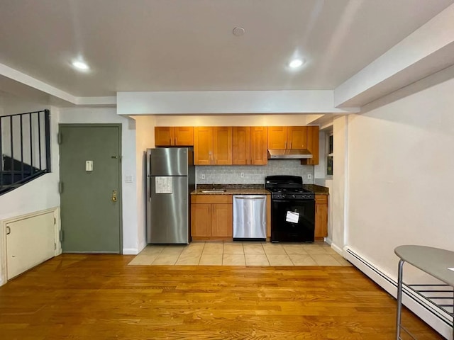 kitchen featuring brown cabinetry, under cabinet range hood, appliances with stainless steel finishes, a baseboard heating unit, and dark countertops