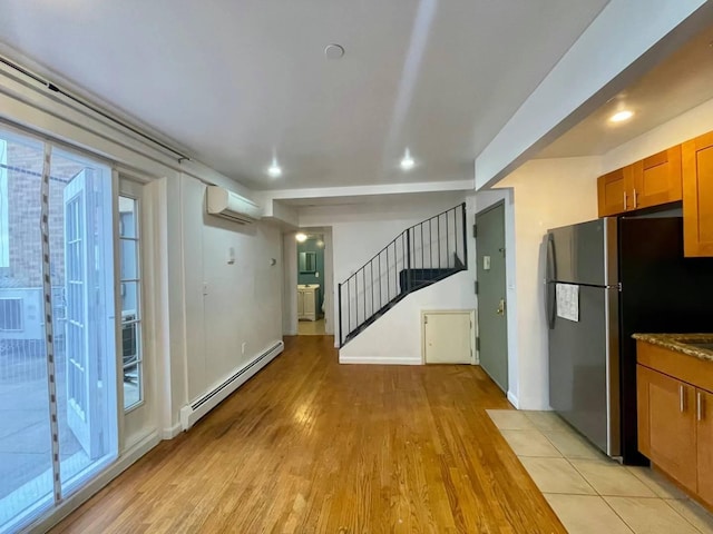 kitchen with a wall unit AC, baseboard heating, freestanding refrigerator, light wood-style floors, and brown cabinetry