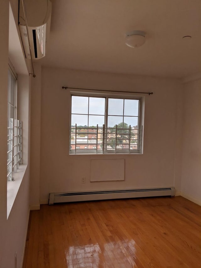 unfurnished room with a baseboard heating unit, baseboards, and wood finished floors