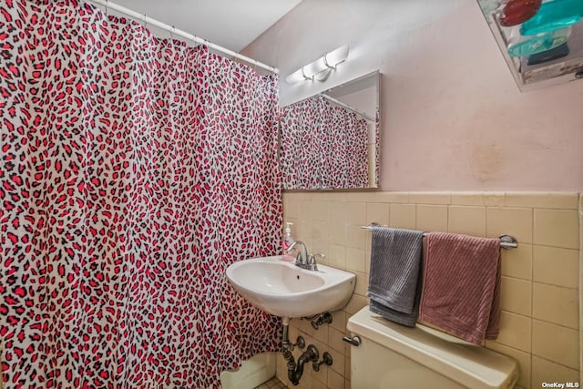 bathroom with a shower with curtain, toilet, a sink, tile walls, and wainscoting