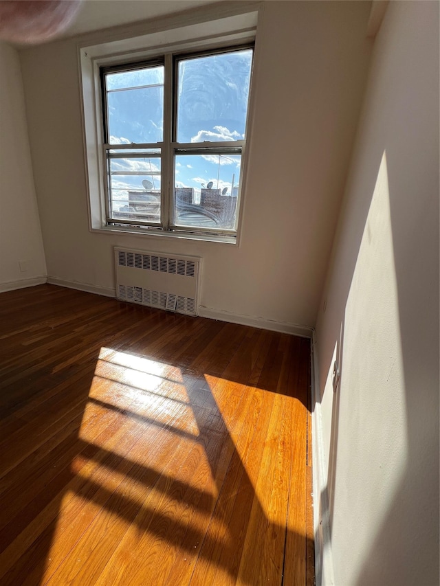 empty room featuring radiator, baseboards, and hardwood / wood-style flooring