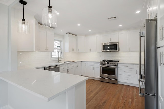 kitchen featuring appliances with stainless steel finishes, a peninsula, wood finished floors, white cabinets, and a sink