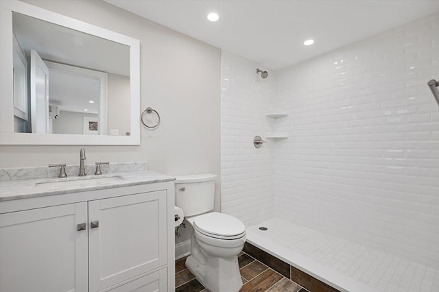 bathroom with wood finish floors, toilet, vanity, and a tile shower