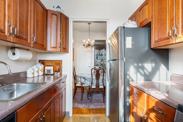 kitchen featuring dark countertops, brown cabinets, freestanding refrigerator, a notable chandelier, and a sink