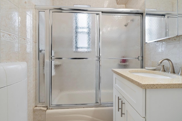 full bathroom featuring bath / shower combo with glass door, tile walls, and vanity