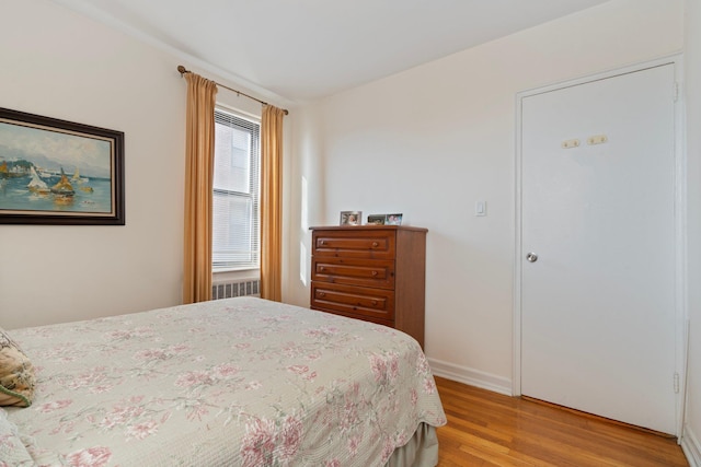 bedroom featuring baseboards, radiator, and light wood finished floors