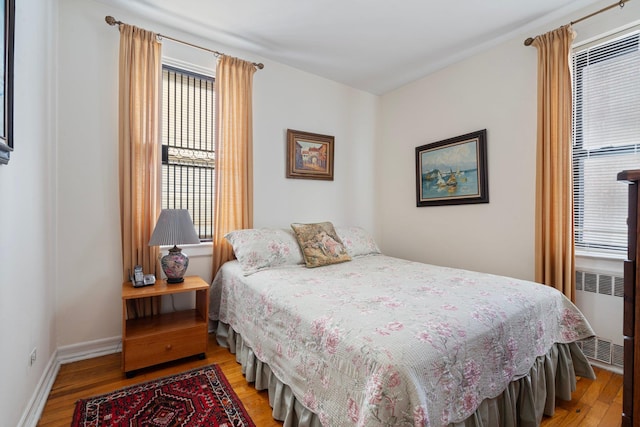 bedroom with radiator, light wood-style floors, and baseboards