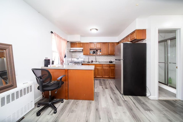 kitchen with under cabinet range hood, freestanding refrigerator, radiator, a peninsula, and stove