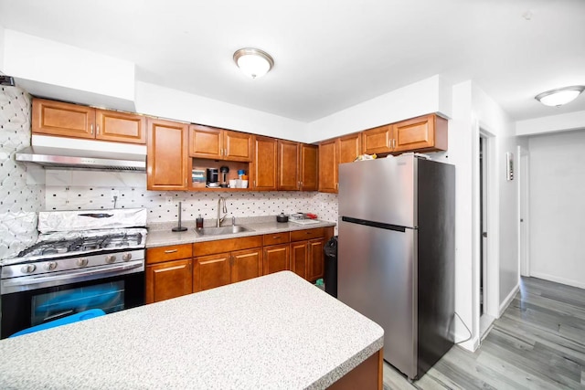 kitchen with a sink, decorative backsplash, light countertops, stainless steel appliances, and under cabinet range hood
