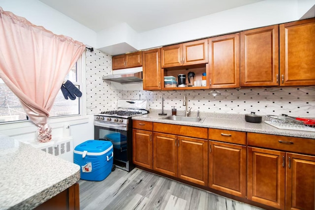 kitchen with under cabinet range hood, radiator heating unit, brown cabinets, stainless steel gas stove, and a sink