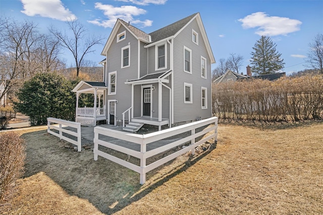 rear view of house featuring a wooden deck, roof with shingles, and fence