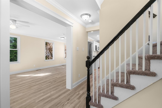 staircase featuring a ceiling fan, crown molding, baseboards, and wood finished floors