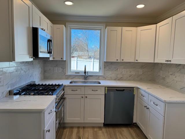 kitchen featuring ornamental molding, appliances with stainless steel finishes, light wood-style floors, white cabinets, and a sink