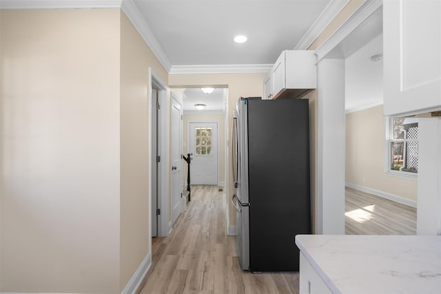 kitchen with white cabinetry, freestanding refrigerator, light wood-style floors, crown molding, and light stone countertops