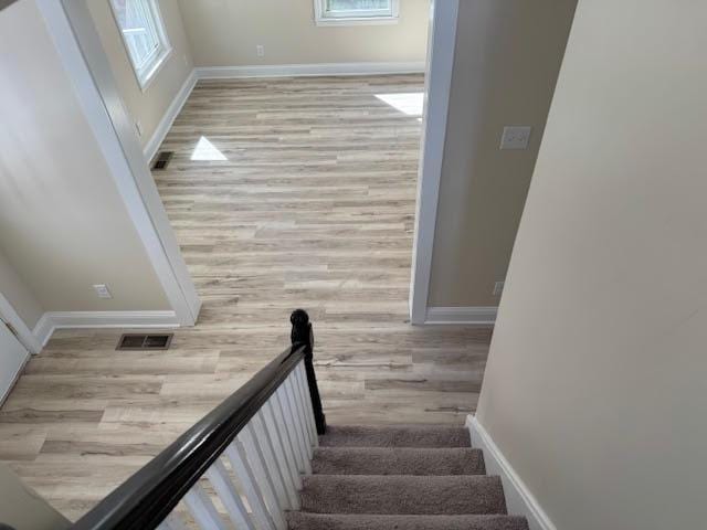 stairway featuring wood finished floors, baseboards, and visible vents