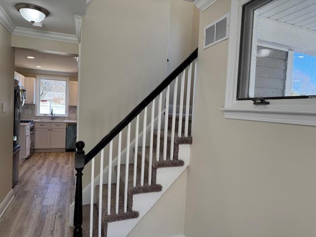 stairway featuring visible vents, wood finished floors, and ornamental molding