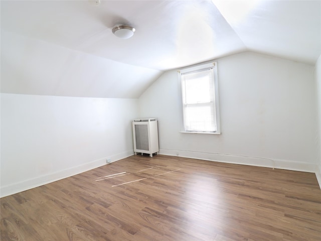 additional living space featuring vaulted ceiling, radiator heating unit, wood finished floors, and baseboards