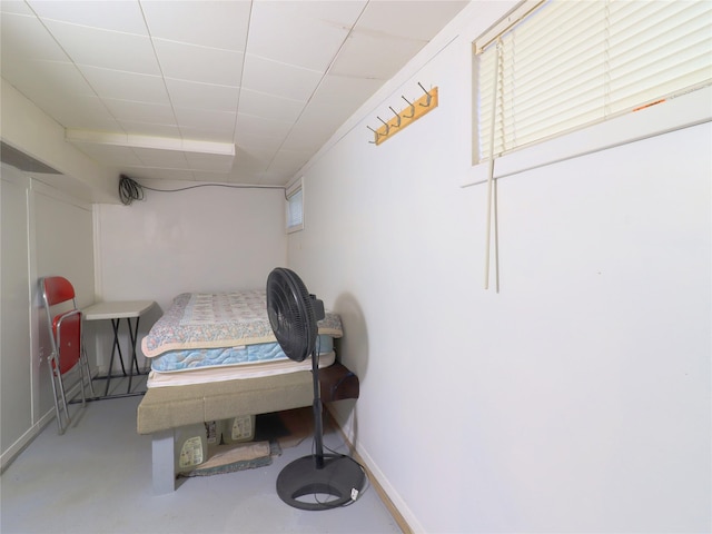 bedroom featuring a drop ceiling, concrete floors, and baseboards