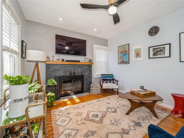 living area featuring baseboards, plenty of natural light, wood finished floors, and a fireplace with flush hearth