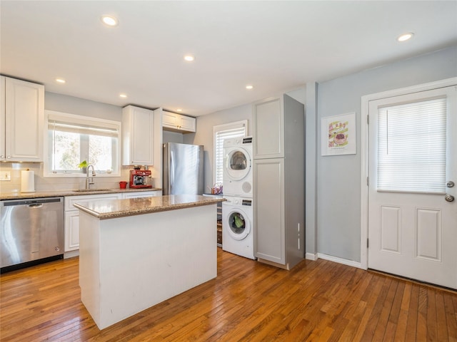 kitchen with light wood finished floors, a sink, stainless steel appliances, stacked washer and dryer, and a center island