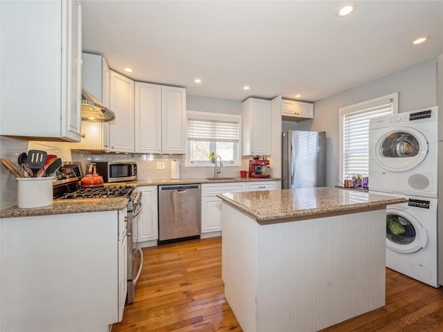 kitchen with light wood-type flooring, a sink, stacked washing maching and dryer, appliances with stainless steel finishes, and white cabinets