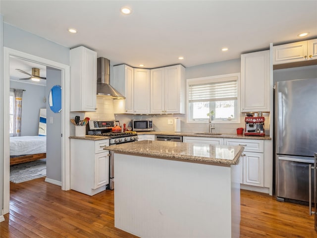 kitchen with white cabinetry, wall chimney exhaust hood, wood finished floors, and stainless steel appliances