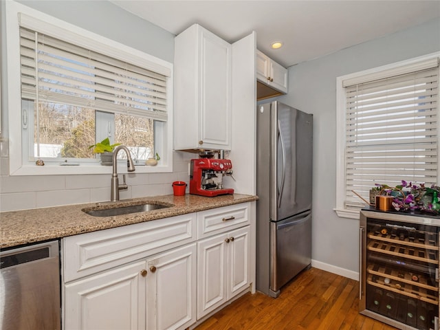 kitchen featuring beverage cooler, a sink, decorative backsplash, white cabinets, and appliances with stainless steel finishes