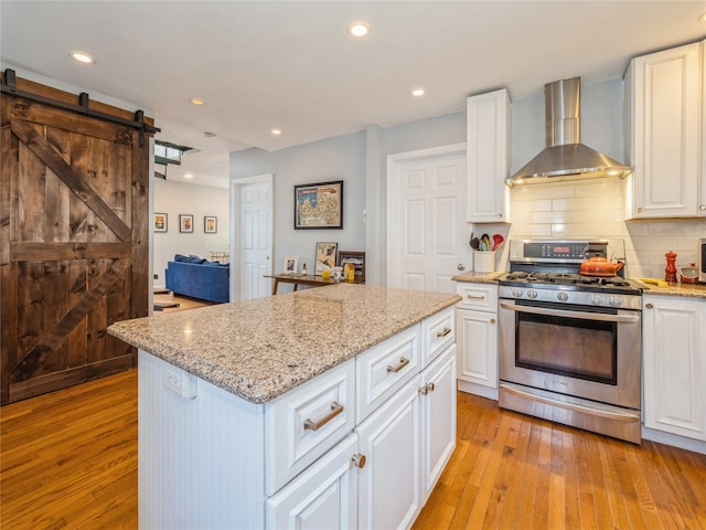 kitchen with gas stove, light wood finished floors, a barn door, wall chimney exhaust hood, and tasteful backsplash