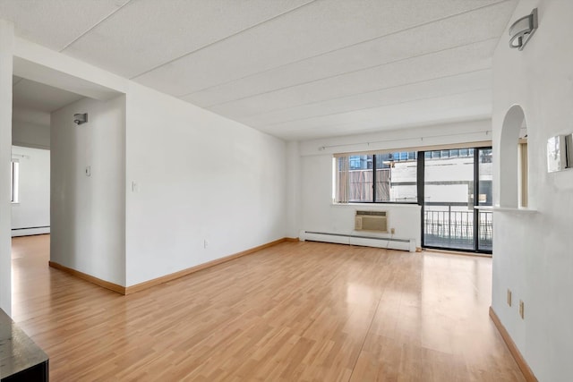 unfurnished room with baseboards, light wood-type flooring, baseboard heating, and arched walkways