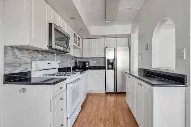 kitchen with a sink, appliances with stainless steel finishes, white cabinetry, dark countertops, and backsplash