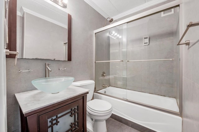 bathroom featuring toilet, vanity, ornamental molding, shower / bath combination with glass door, and tile walls