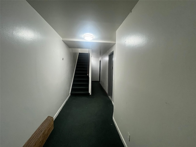 hall with stairway, baseboards, and dark colored carpet