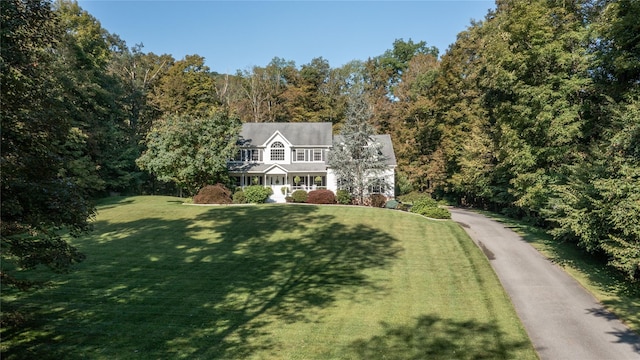 view of front of house featuring aphalt driveway, a wooded view, and a front yard