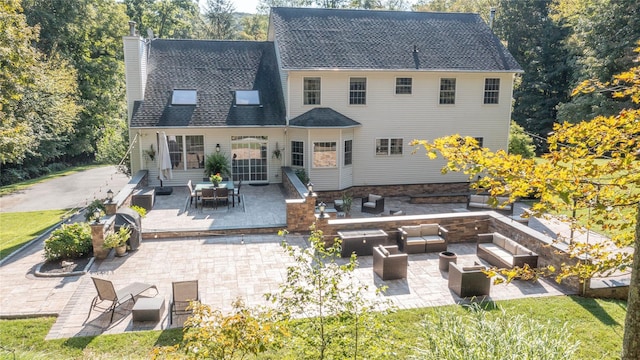 rear view of property featuring an outdoor living space with a fire pit, a patio, roof with shingles, and a chimney