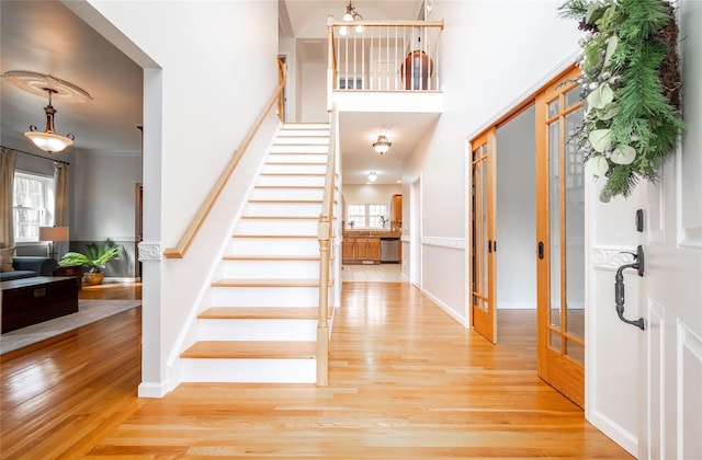 entryway with stairway, baseboards, light wood-style flooring, a towering ceiling, and crown molding