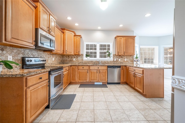 kitchen featuring a sink, light stone counters, appliances with stainless steel finishes, a peninsula, and decorative backsplash