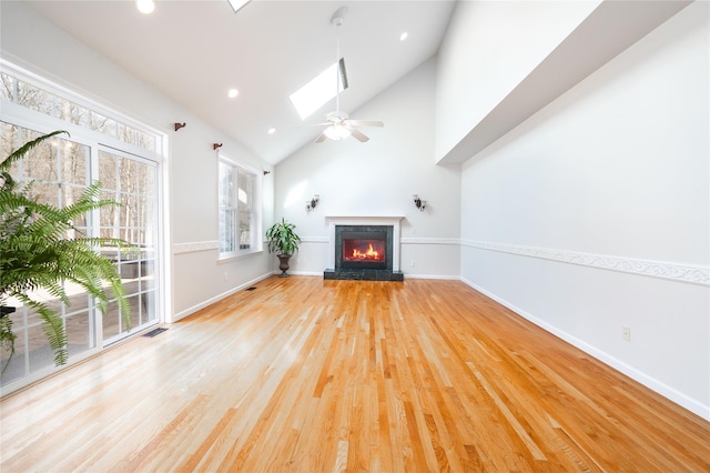 unfurnished living room featuring visible vents, light wood-style flooring, a lit fireplace, a skylight, and baseboards