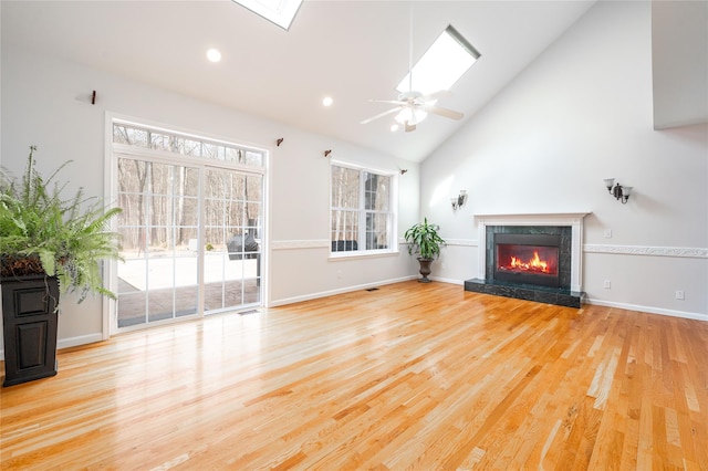 unfurnished living room with a high end fireplace, high vaulted ceiling, a skylight, and wood finished floors