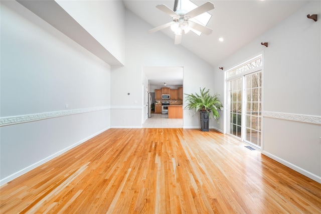 empty room featuring visible vents, high vaulted ceiling, a ceiling fan, light wood finished floors, and baseboards