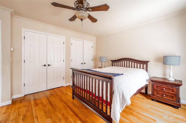 bedroom with wood finished floors, baseboards, ceiling fan, crown molding, and two closets