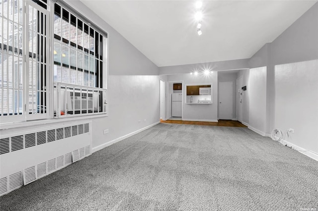 carpeted spare room featuring baseboards, radiator, and vaulted ceiling