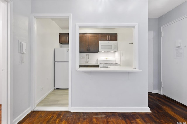 kitchen featuring wood finished floors, white appliances, dark brown cabinetry, light countertops, and baseboards