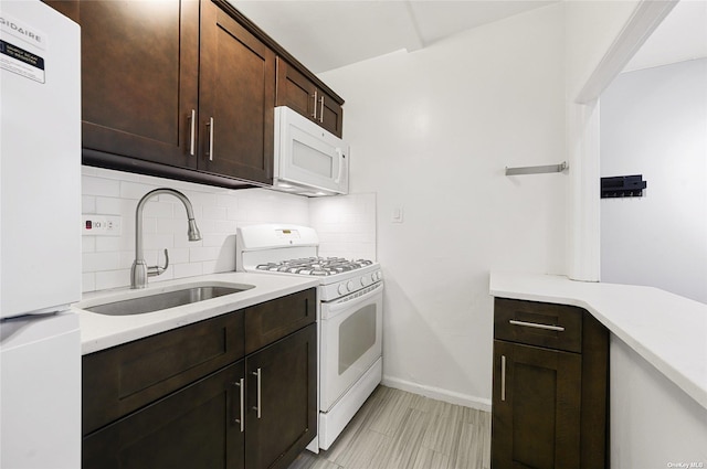 kitchen with tasteful backsplash, dark brown cabinetry, light countertops, white appliances, and a sink