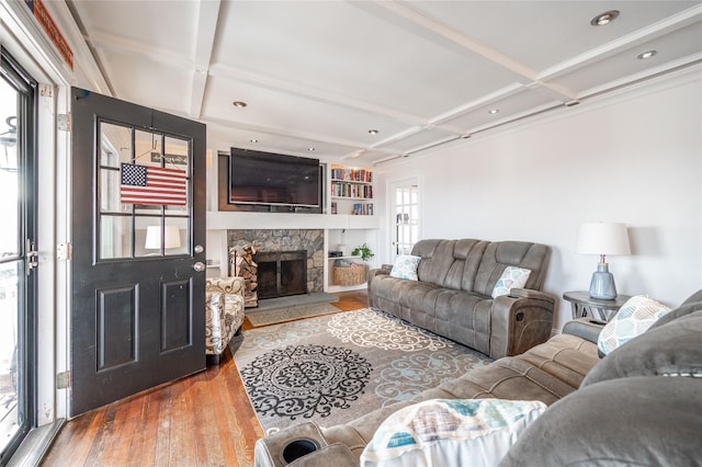 living area with hardwood / wood-style floors, built in shelves, coffered ceiling, beam ceiling, and a stone fireplace