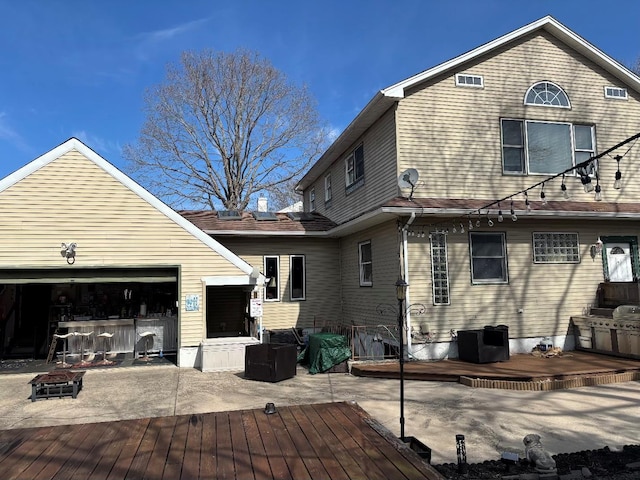 rear view of property featuring a wooden deck, driveway, an outdoor fire pit, and a garage