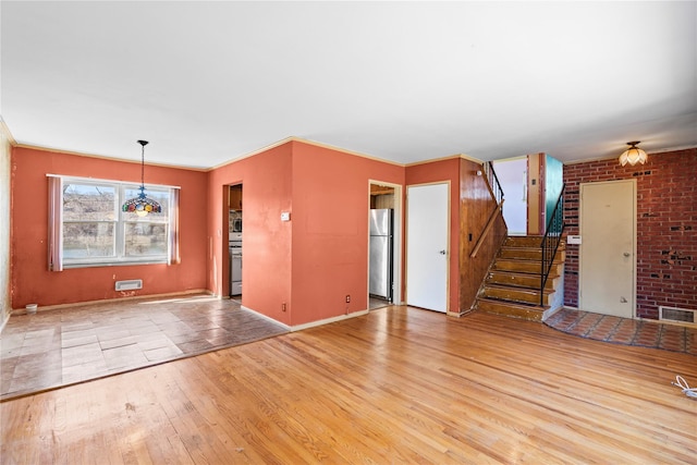 unfurnished living room with stairway, wood finished floors, visible vents, baseboards, and crown molding