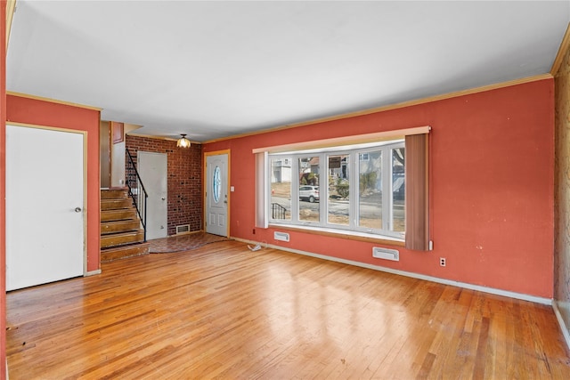 unfurnished living room featuring light wood finished floors, stairway, crown molding, and visible vents