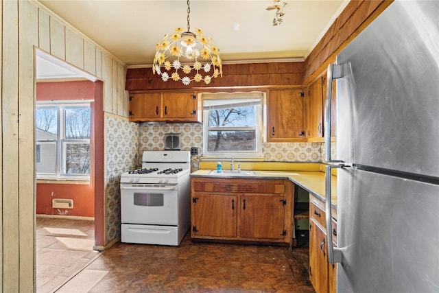 kitchen featuring white range with gas cooktop, freestanding refrigerator, a sink, light countertops, and tasteful backsplash