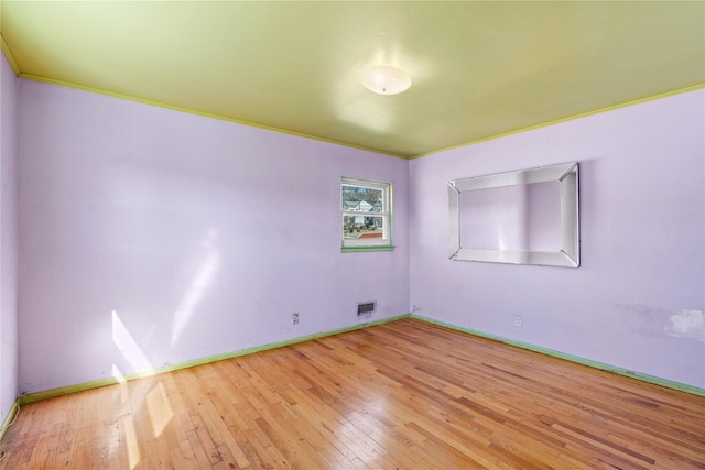 spare room featuring hardwood / wood-style flooring, baseboards, visible vents, and ornamental molding